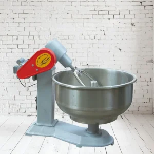 یک دستگاه خمیرگیر صنعتی با کاسه استیل بزرگ، بدنه خاکستری و کاور موتور قرمز، در پس‌زمینه دیوار آجری سفید.